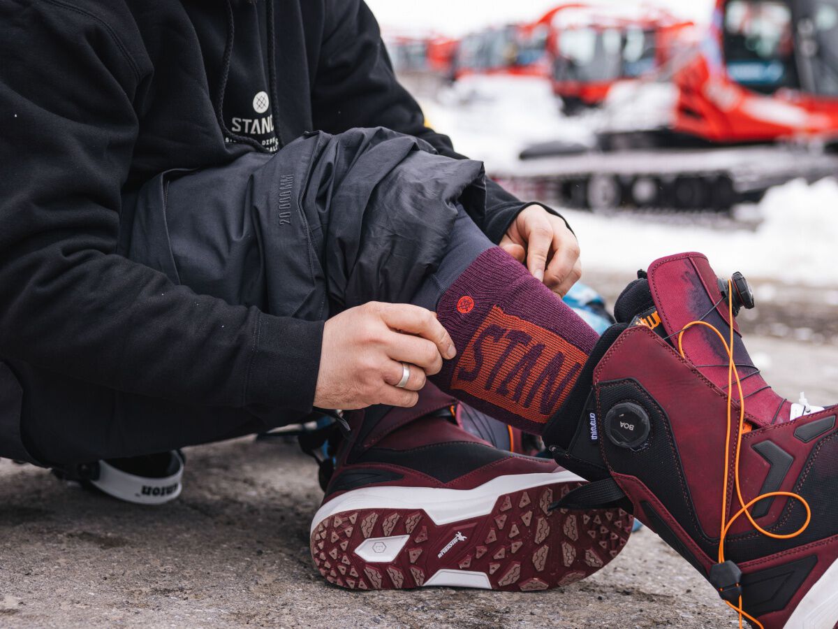 Person putting on red Stance snow socks and red snowboard boots